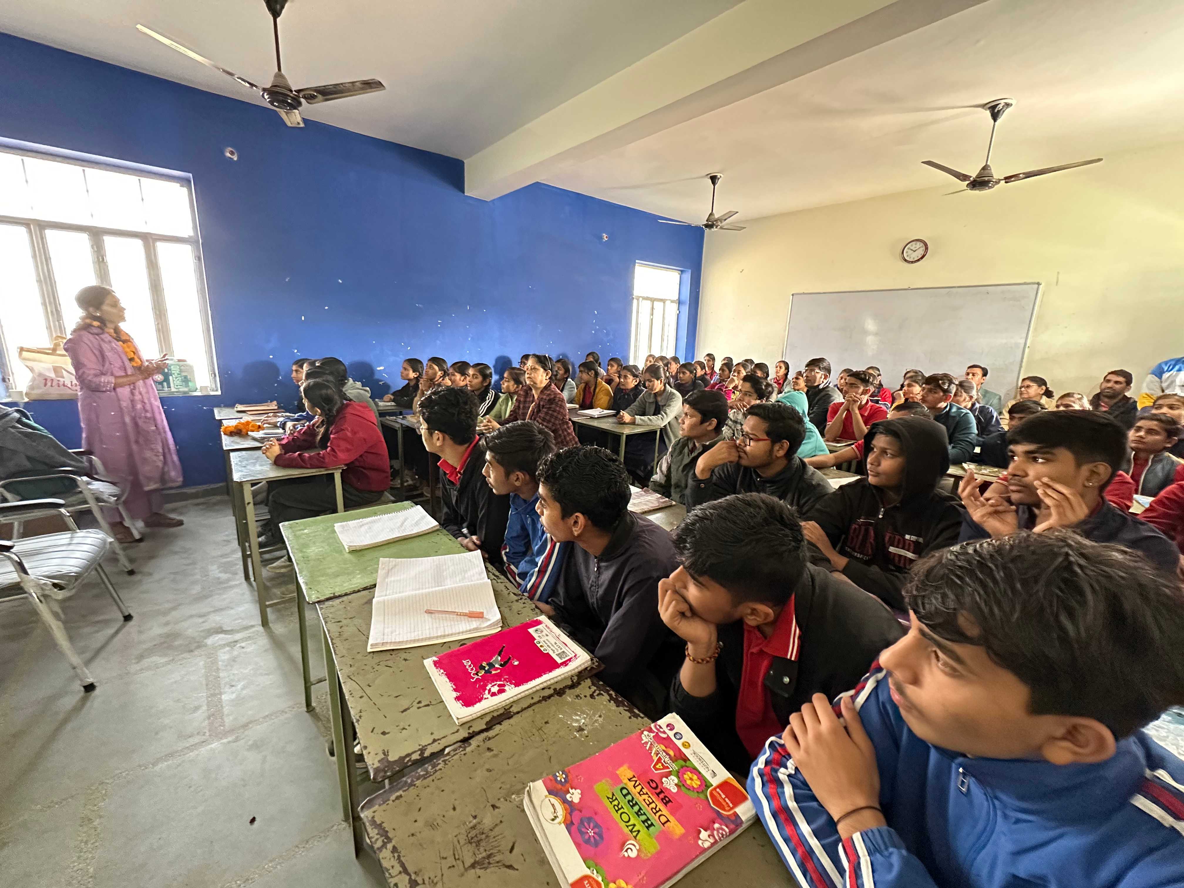 Students attentively listening to an instructor in a classroom with blue walls
